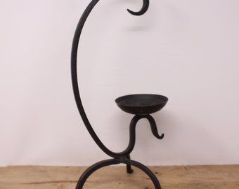 May include: Black metal candle holder with a curved arm and a round base. The holder has a single candle cup.