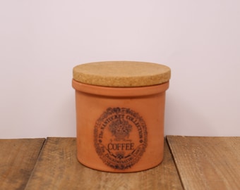 May include: A terracotta coffee canister with a cork lid. The canister has a blue and white label that reads "The Warwick Collection Coffee Decaffeinated".