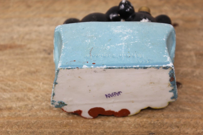 May include: A blue ceramic figurine of Mickey Mouse sitting on a chair. The figurine is marked "&copy; WALT DISNEY" and "JAPAN" on the bottom.