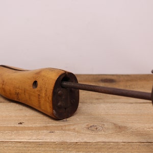 May include: A wooden shoe stretcher with a metal screw and handle. The stretcher is designed to help maintain the shape of shoes.