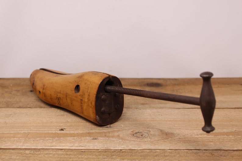May include: A wooden shoe stretcher with a metal screw and handle. The stretcher is designed to help maintain the shape of shoes.