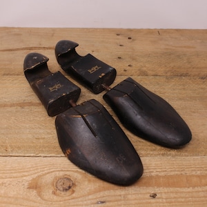 May include: Four vintage black wooden shoe trees with metal hardware. The shoe trees are arranged on a light brown wooden surface. The shoe trees have the word "Toeley" printed on them.