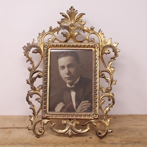 May include: An ornate gold-toned picture frame with a black and white photograph of a man wearing a suit and tie.