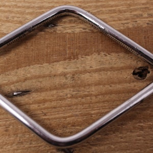 May include: A silver metal tool with a square shape and a handle with a bend. The tool has a small knob on one end.