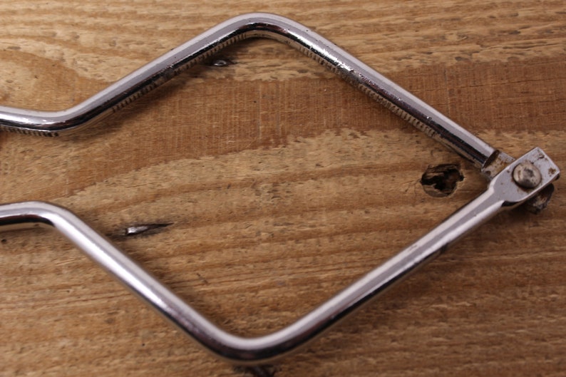 May include: A silver metal tool with a square shape and a handle with a bend. The tool has a small knob on one end.