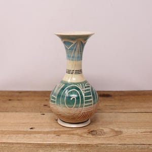May include: A decorative ceramic vase with a bulbous body and flared neck. The vase features a teal, cream, and brown colour scheme with geometric and spiral designs. The base is a small, circular shape.