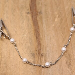 May include: A silver chain with five white pearl beads and two silver clips at each end.