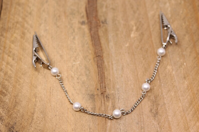 May include: A silver chain with five white pearl beads and two silver clips at each end.