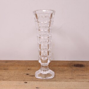 May include: A clear glass vase with a square patterned design. The vase has a tall, slender body and a square base.