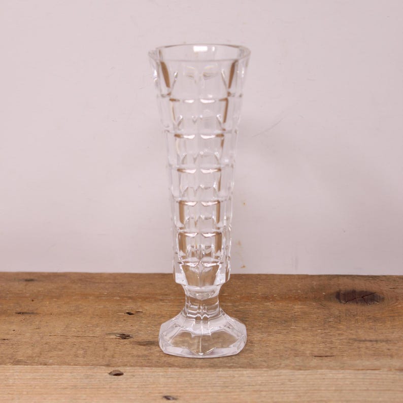 May include: A clear glass vase with a square patterned design. The vase has a tall, slender body and a square base.