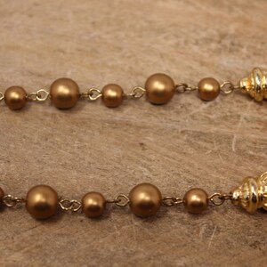 May include: A gold-toned necklace with a chain and large round beads. The necklace has two gold-toned tassels at the ends.