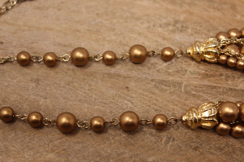 May include: A gold-toned necklace with a chain and large round beads. The necklace has two gold-toned tassels at the ends.