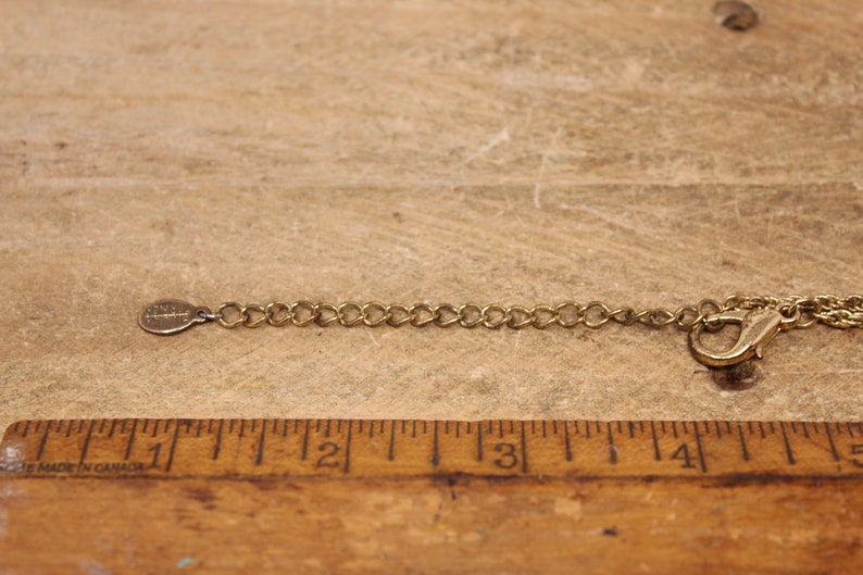 May include: A gold chain necklace with a lobster clasp closure. The chain is made of small, linked circles. The chain is measured against a wooden ruler.