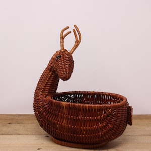May include: A brown wicker basket shaped like a deer with antlers. The basket is sitting on a wooden surface.