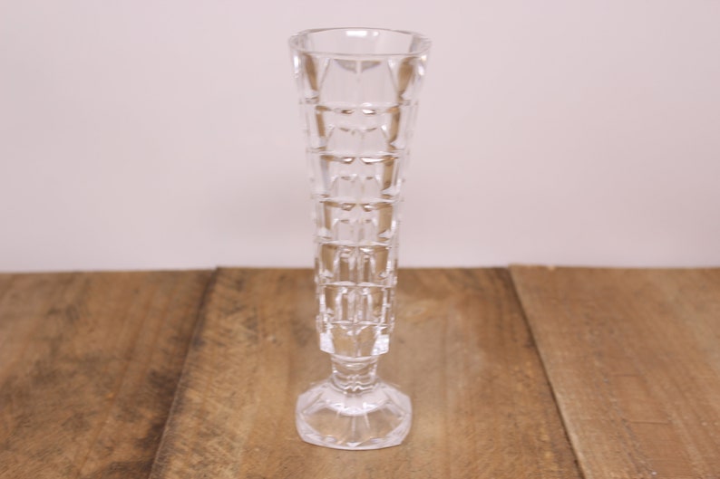 May include: A clear glass vase with a geometric pattern. The vase has a tall, slender body and a wide base.