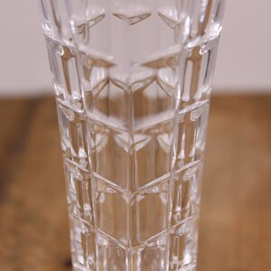 May include: A clear glass vase with a geometric pattern. The vase is tall and slender, with a square base.