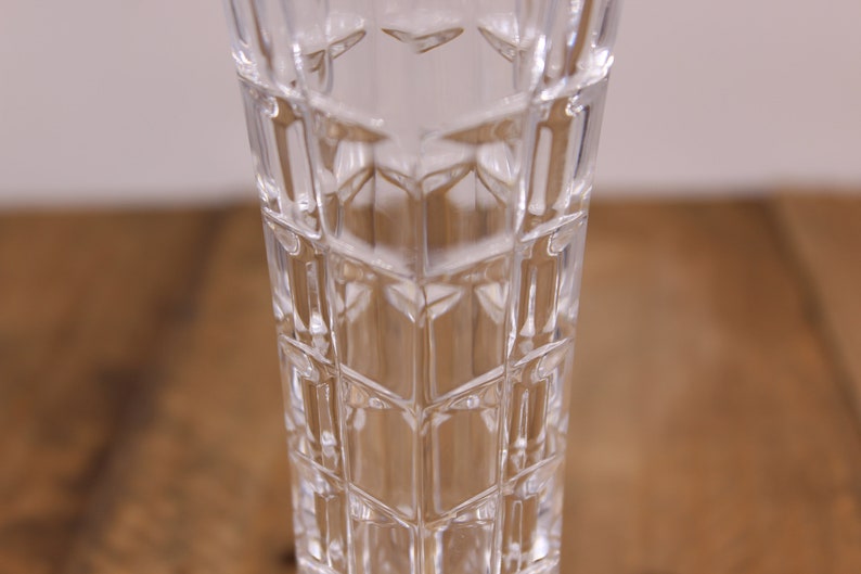 May include: A clear glass vase with a geometric pattern. The vase is tall and slender, with a square base.