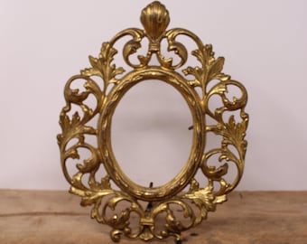 Può includere: Una cornice per foto in metallo dorato con un design ornato e arrotolato. La cornice è di forma ovale e ha un supporto sul retro.