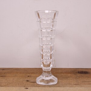 May include: A clear glass vase with a square patterned design. The vase has a tall, slender body and a square base.