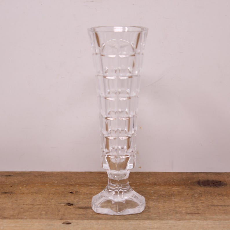 May include: A clear glass vase with a square patterned design. The vase has a tall, slender body and a square base.