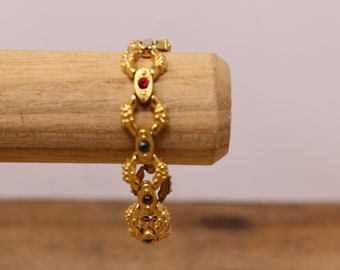 May include: A gold bracelet with a chain link design and red, green, and blue gemstones.