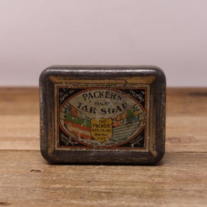 May include: Aged tin of Packer's Tar Soap. The rectangular tin shows signs of wear. The label displays the text "Packer's Tar Soap" and "The Packer Mfg. Co. Inc. New York, U.S.A.", along with illustrations of flags and ships.