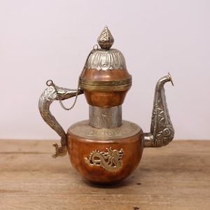 May include: A silver and copper teapot with a dragon design. The teapot has a hinged lid and a chain handle. The spout is shaped like a dragon's head.