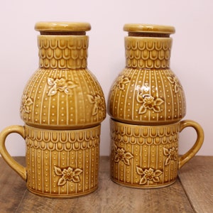May include: Two ceramic teapots with lids and matching mugs. The teapots and mugs are brown with a white floral pattern.