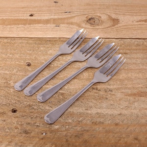 May include: Four stainless steel forks arranged diagonally on a wooden surface. Each fork has four tines and a rounded handle. The forks are evenly spaced and reflect the light, creating a clean and modern aesthetic. The wooden surface has a warm, natural tone.