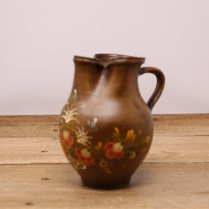 May include: A small brown ceramic pitcher with a floral design painted in yellow, orange, and green. The pitcher has a unique double spout and a handle.
