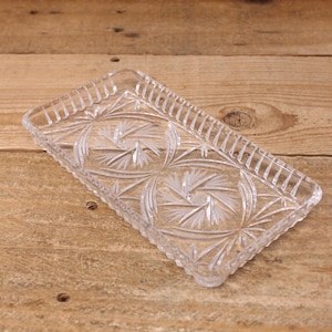 Peut inclure: Un plateau rectangulaire en verre transparent avec un motif détaillé d'éclats d'étoiles et d'éventails. Le plateau a une bordure décorative et nervurée et est surélevé par de petits pieds. Le verre est transparent, laissant passer la lumière.