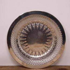 May include: A silver-toned metal dish with a decorative, embossed design. The dish has a circular shape and a raised rim.