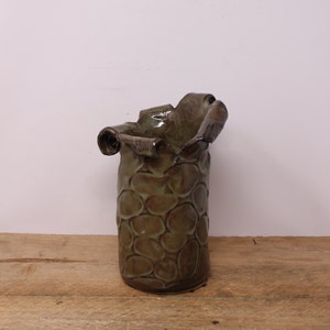 May include: A green ceramic vase with a textured, organic design. The vase has a wide opening and a narrow base.