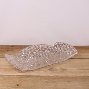 May include: A clear glass serving tray with a decorative, raised, diamond-shaped pattern. The tray has a slightly curved shape.
