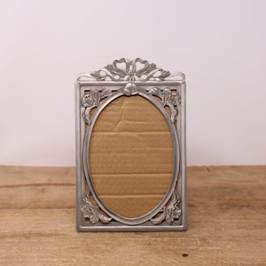 May include: A silver picture frame with an ornate design featuring a bow and floral accents. The frame is empty and ready to hold a photo.