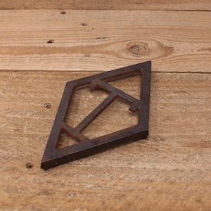 May include: A diamond-shaped, rusty brown metal object with an openwork design. The geometric shape features a central T-shaped element and angled lines, likely a decorative or functional piece.