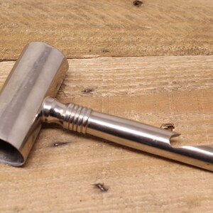 May include: A silver metal bottle opener with a long handle and a rounded end. The opener has a small, circular hole on the side.