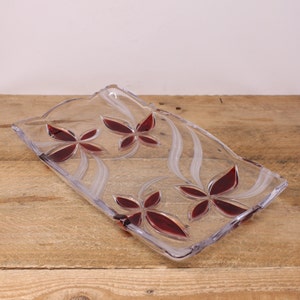 May include: A clear glass serving tray with a wavy design and four red floral accents.