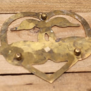 May include: A brass heart-shaped coaster featuring two birds in flight, a cut-out design, and three decorative rivets.