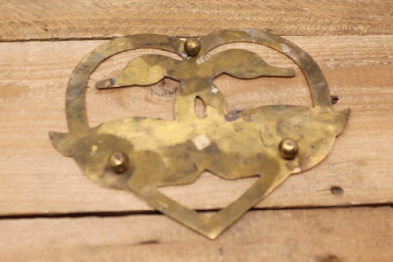 May include: A brass heart-shaped coaster featuring two birds in flight, a cut-out design, and three decorative rivets.