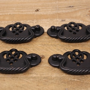 May include: Four black metal cabinet drawer pulls with a decorative, intricate design. Each pull has a rope-like edge and a center design that resembles a knot or a woven pattern.