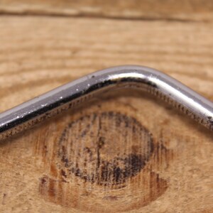 May include: Close-up of a silver metal wrench with a 90-degree bend.