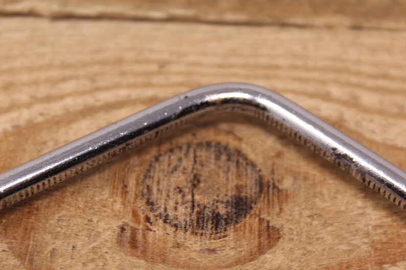 May include: Close-up of a silver metal wrench with a 90-degree bend.