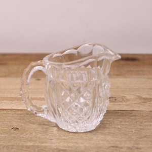 May include: A clear glass jug with a diamond pattern. The jug has a handle and a spout.