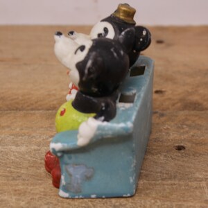 May include: A vintage ceramic figurine of Mickey Mouse and Minnie Mouse sitting on a blue couch. The figurine is painted in black, white, yellow, and red.