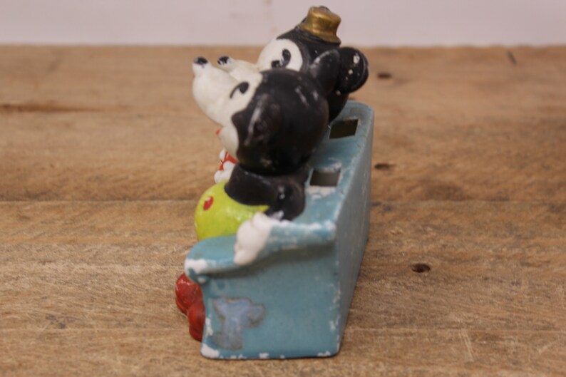 May include: A vintage ceramic figurine of Mickey Mouse and Minnie Mouse sitting on a blue couch. The figurine is painted in black, white, yellow, and red.