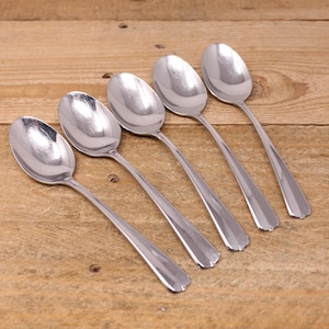 May include: Five silver spoons with rounded bowls and slightly curved handles. The spoons are arranged in a row on a wooden surface.