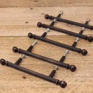 May include: Five black cabinet knobs with a fluted design and a rounded knob on each end. The knobs are arranged in a staggered pattern on a wooden surface.