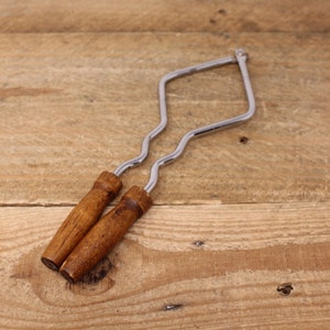 May include: A metal grilling tool with wooden handles. The tool is shaped like a diamond and has a curved design. It is used to lift and turn food on a grill.