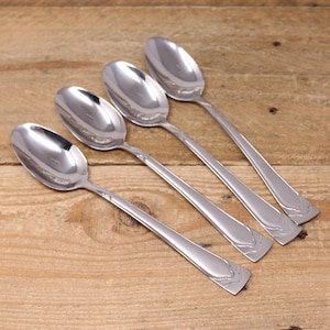May include: Four silver spoons with ornate handles. The spoons are arranged in a row on a wooden surface.